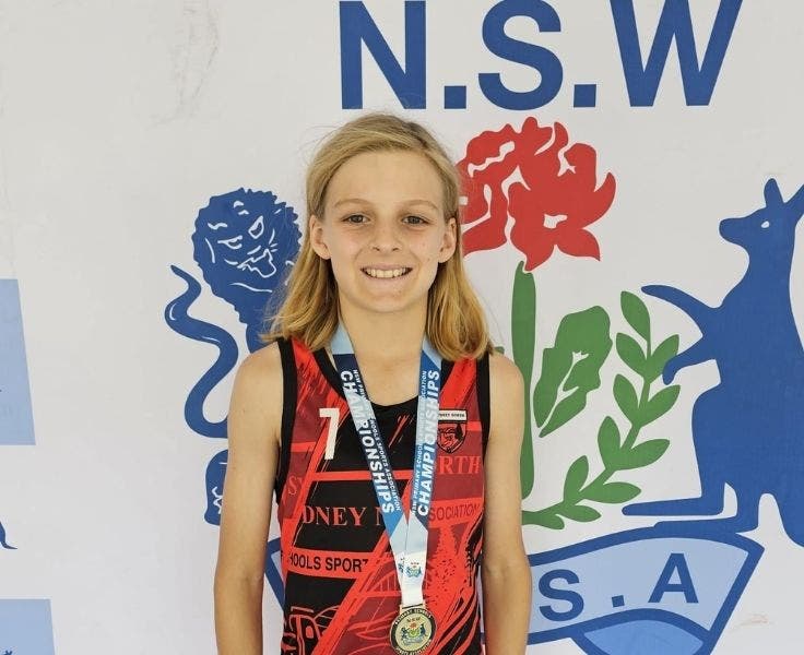 Male student with medal hanging around his neck in front of NSW emblem