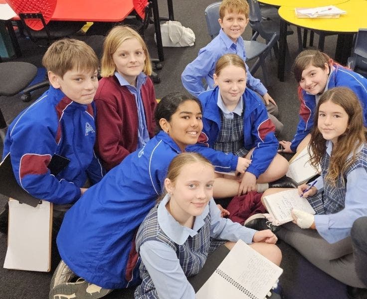 Group of students sitting on floor with notebooks in hand.