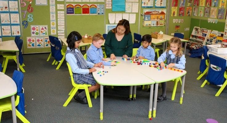 Teacher sitting with 4 students playing with blocks on table